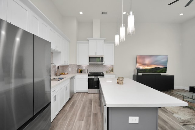 kitchen featuring stainless steel appliances, a kitchen island, a sink, light countertops, and tasteful backsplash