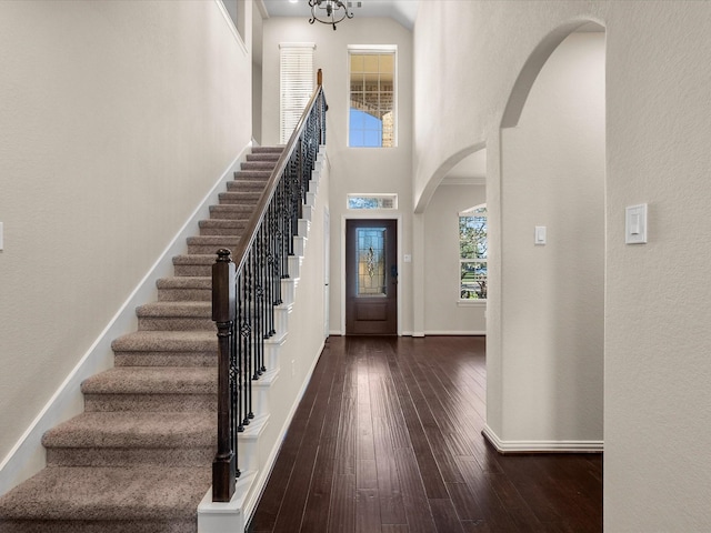 entrance foyer featuring arched walkways, a high ceiling, baseboards, stairway, and hardwood / wood-style floors