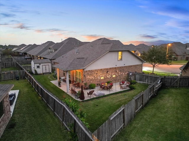 back of property at dusk with brick siding, a fenced backyard, an outbuilding, and a patio