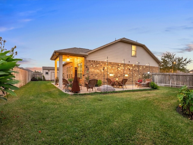 back of property at dusk with a patio area, a fenced backyard, a lawn, and brick siding