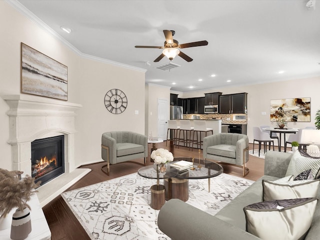 living room with recessed lighting, wood finished floors, visible vents, ornamental molding, and a glass covered fireplace