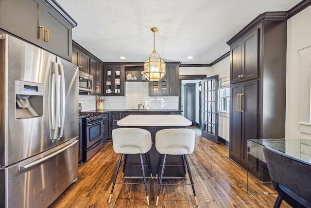 kitchen featuring a center island, appliances with stainless steel finishes, decorative backsplash, dark wood finished floors, and glass insert cabinets