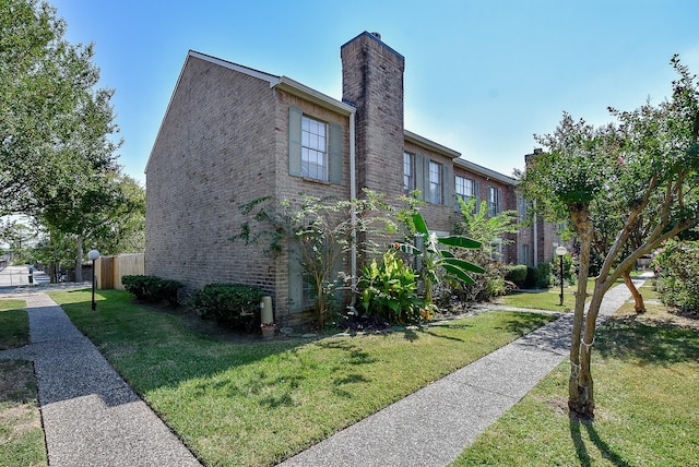 view of side of property with brick siding, a yard, a chimney, and fence