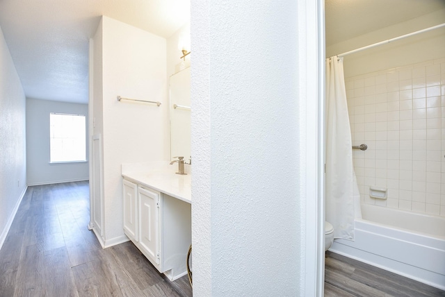 bathroom with a textured wall, toilet, vanity, wood finished floors, and baseboards