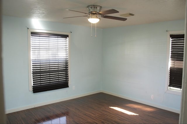 empty room featuring dark wood-style floors, visible vents, ceiling fan, and baseboards