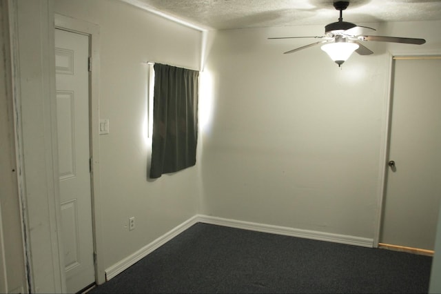 empty room with a textured ceiling, dark carpet, a ceiling fan, and baseboards