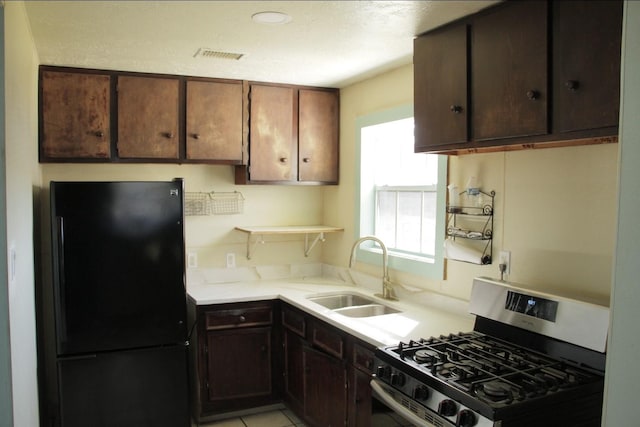 kitchen featuring light countertops, freestanding refrigerator, a sink, dark brown cabinetry, and stainless steel gas range