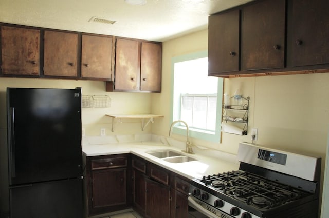 kitchen with light countertops, visible vents, freestanding refrigerator, a sink, and stainless steel gas range