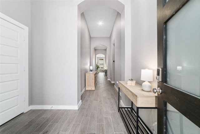 corridor with arched walkways, baseboards, and wood finished floors