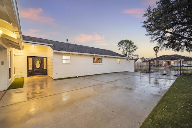 view of property exterior with a patio area, fence, brick siding, and roof with shingles