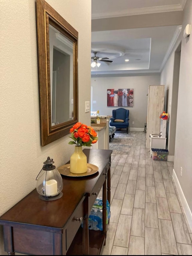 hallway featuring baseboards, a tray ceiling, wood finish floors, and crown molding