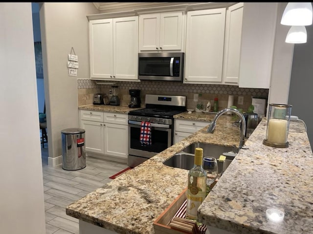 kitchen featuring light stone counters, stainless steel appliances, a sink, white cabinets, and tasteful backsplash