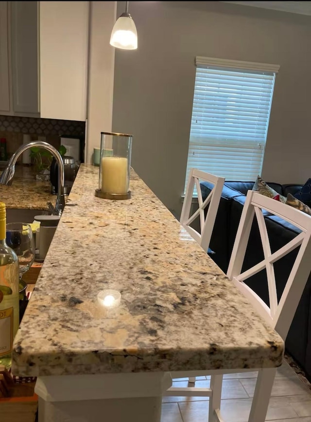 kitchen with light stone counters, a sink, white cabinets, hanging light fixtures, and tasteful backsplash