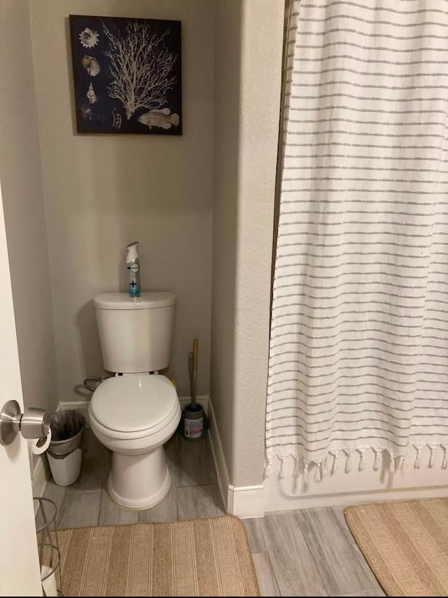 full bath featuring a shower with shower curtain, baseboards, toilet, and wood finished floors