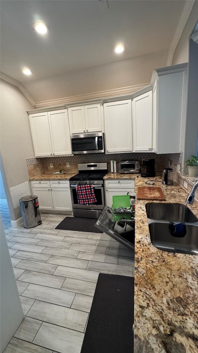 kitchen featuring light stone counters, stainless steel appliances, a sink, white cabinetry, and backsplash