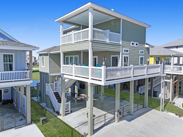 rear view of property with a lawn, concrete driveway, a balcony, stairs, and a carport