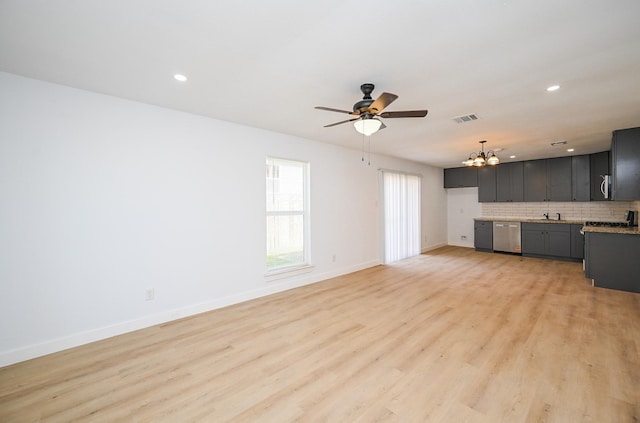unfurnished living room with ceiling fan with notable chandelier, a sink, visible vents, baseboards, and light wood-type flooring