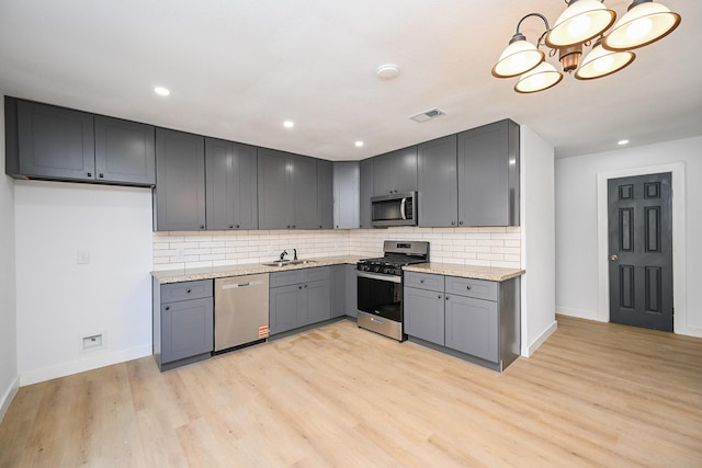 kitchen featuring visible vents, appliances with stainless steel finishes, gray cabinetry, light wood-type flooring, and a sink