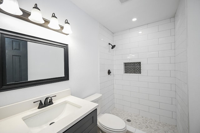 bathroom with a tile shower, vanity, and toilet