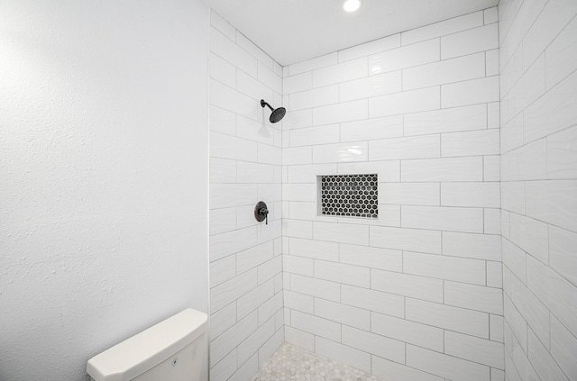 full bathroom with a tile shower and toilet