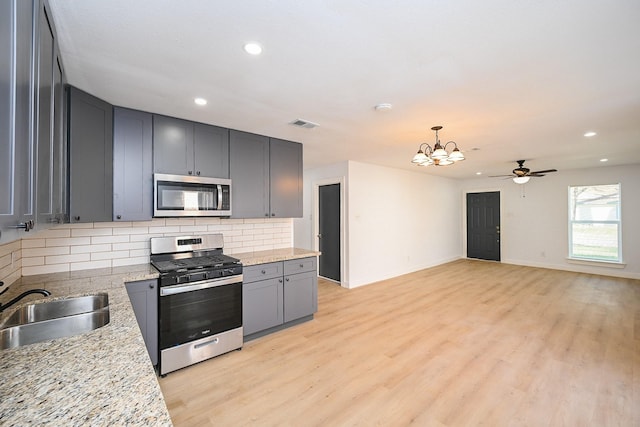 kitchen featuring tasteful backsplash, appliances with stainless steel finishes, gray cabinets, light wood-style floors, and a sink