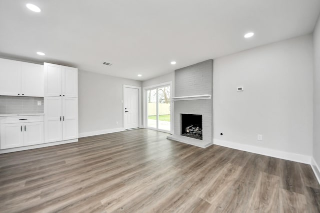 unfurnished living room featuring light wood-style floors, baseboards, a brick fireplace, and visible vents