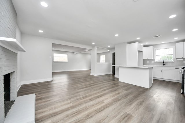 unfurnished living room featuring recessed lighting, visible vents, a brick fireplace, a sink, and wood finished floors