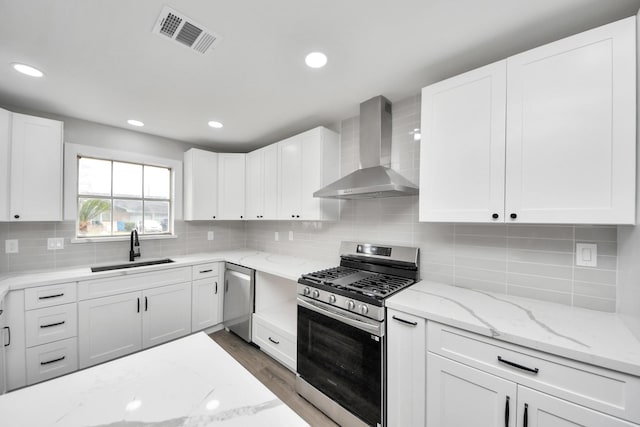 kitchen with stainless steel appliances, visible vents, white cabinetry, a sink, and wall chimney exhaust hood