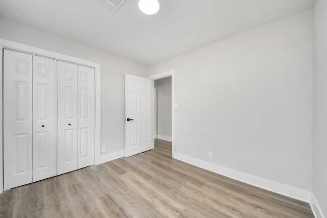 unfurnished bedroom with baseboards, a closet, visible vents, and wood finished floors