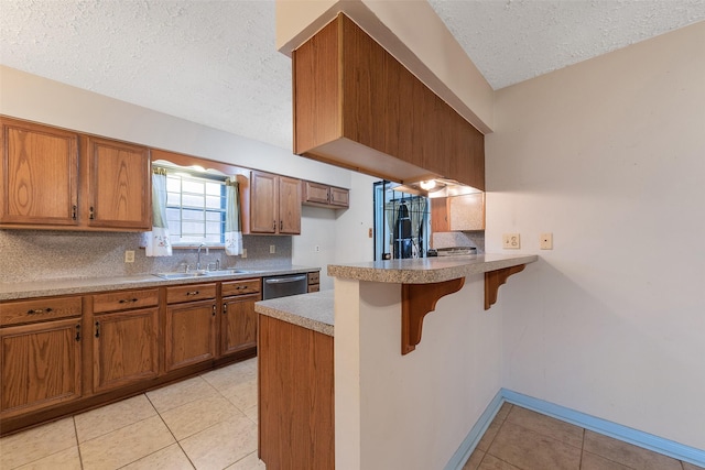 kitchen featuring a peninsula, a sink, stainless steel dishwasher, brown cabinets, and tasteful backsplash