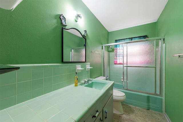 full bath with tile walls, toilet, enclosed tub / shower combo, vanity, and tile patterned floors