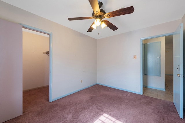 unfurnished bedroom featuring carpet floors, a spacious closet, baseboards, and a ceiling fan