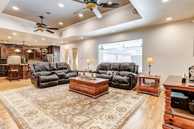 living area featuring a tray ceiling, light wood-style floors, visible vents, and ornamental molding