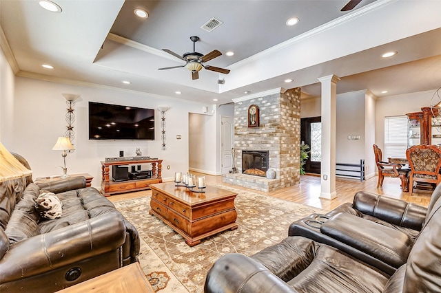 living room with visible vents, light wood-style flooring, a fireplace, decorative columns, and ceiling fan