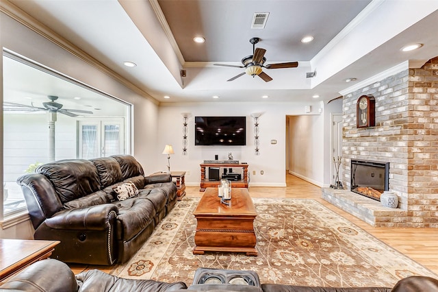 living room with visible vents, a brick fireplace, ornamental molding, wood finished floors, and a raised ceiling