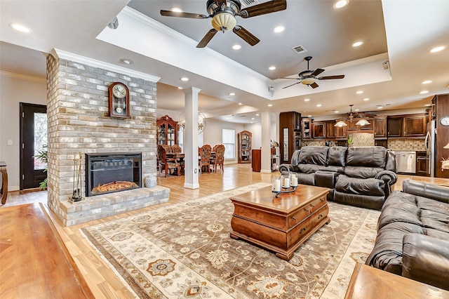 living area with light wood-type flooring, visible vents, a tray ceiling, crown molding, and ornate columns