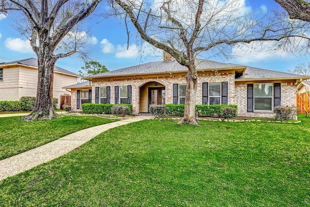 view of front of house featuring brick siding, roof with shingles, a front lawn, and fence