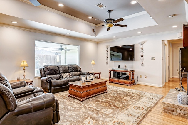 living room with light wood finished floors, visible vents, ceiling fan, a tray ceiling, and ornamental molding