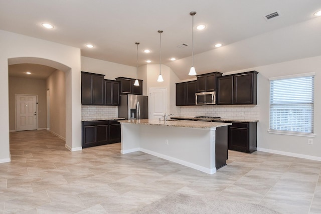 24703 Heirloom Ln, Katy, TX 77493 - kitchen featuring stainless steel appliances, arched walkways, decorative backsplash, light stone countertops, and a kitchen island with sink