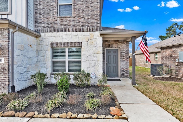 property entrance with stone siding, central AC unit, and brick siding