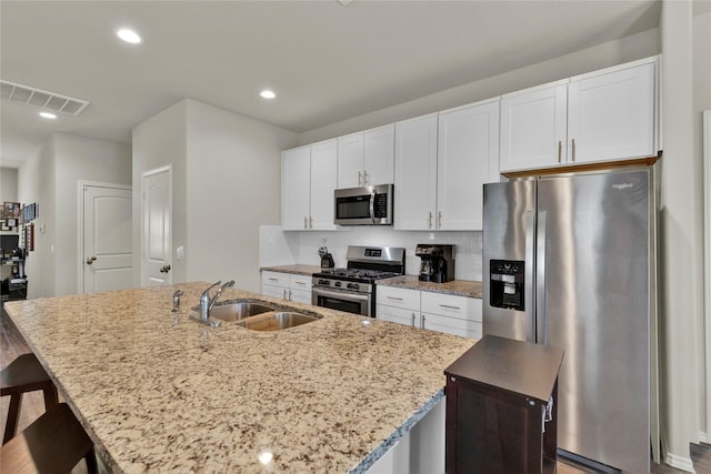 kitchen featuring visible vents, an island with sink, appliances with stainless steel finishes, white cabinetry, and a sink