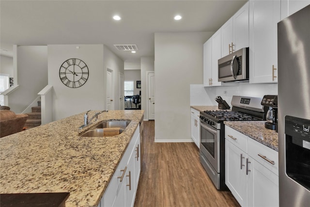 kitchen featuring visible vents, light stone counters, wood finished floors, stainless steel appliances, and a sink