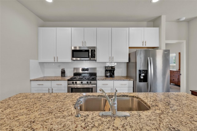 kitchen with decorative backsplash, light stone countertops, stainless steel appliances, white cabinetry, and a sink