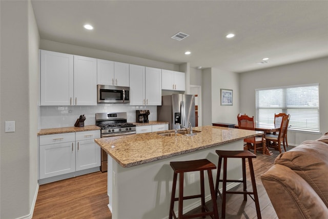 kitchen with visible vents, a breakfast bar area, wood finished floors, stainless steel appliances, and a sink