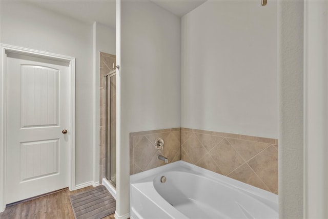 full bathroom featuring a stall shower, a garden tub, and wood finished floors