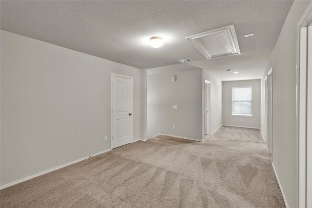 empty room with attic access, light carpet, a textured ceiling, and baseboards