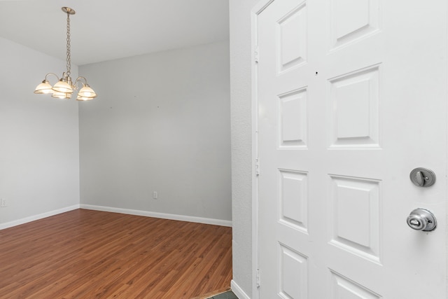 empty room featuring baseboards, wood finished floors, and an inviting chandelier