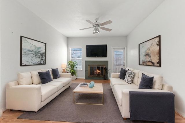 living room with light wood-type flooring, baseboards, a ceiling fan, and a tile fireplace