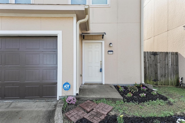 entrance to property with a garage, concrete driveway, fence, and stucco siding