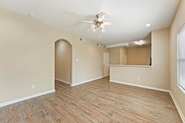 empty room featuring arched walkways, light wood finished floors, visible vents, and baseboards